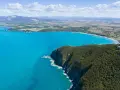 Vista aerea della costa degli Etruschi con mare azzurro, scogliere verdi e un borgo storico.