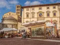 Mercatino d'antiquariato in piazza Grande ad Arezzo, con opere d'arte, sculture e mobili esposti sotto il sole.