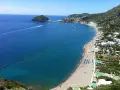 Vista panoramica della spiaggia dei Maronti, con il mare blu intenso, tante barche e la costa verdeggiante.
