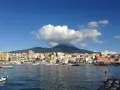 Vista del porto di Torre del Greco con il Vesuvio sullo sfondo, sotto un cielo azzurro con nuvole bianche.