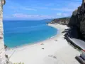 Spiaggia bianca e mare cristallino sulla **Costa degli Dei**. Case aggrappate alla scogliera, una strada panoramica e bagnanti che si godono il sole.