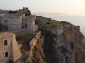Il complesso monumentale del castello di Milazzo si erge su una scogliera a picco sul mare, con torri e mura antiche che dominano il paesaggio.