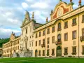 La maestosa Certosa di Calci, con la sua facciata imponente e il prato verde antistante, incanta sotto un cielo nuvoloso.