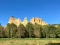 Le maestose balze del Valdarno si ergono sotto un cielo azzurro, circondate da una rigogliosa vegetazione e cipressi slanciati.