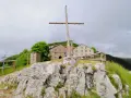 Croce di legno a San Pellegrino in Alpe, con edifici storici sullo sfondo e rocce in primo piano.