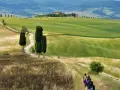 Sentiero tortuoso nel Val d'Orcia, con colline verdi, cipressi e un casale in lontananza. Una mappa ideale per un'escursione.