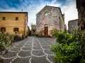 Piazza di Bibbona, cosa vedere: chiesa in pietra con rosone, case gialle e pavimentazione a ventaglio.
