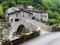 Ponte in pietra a Vergemoli, con case in pietra e vegetazione lussureggiante sullo sfondo. Le antiche fabbriche di Vergemoli sembrano emergere dalla collina.