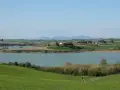 Campagna toscana con lago e casale in collina, un luogo dove la **santa luce cosa vedere** è ovunque, tra dolci pendii verdi e il cielo azzurro.