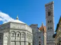 La piazza del Duomo a Firenze con il Battistero, il Campanile di Giotto e la cupola del Brunelleschi sotto un cielo azzurro.