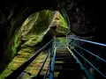 Una scala metallica sale tra le rocce muschiose degli orridi di Uriezzo, illuminata da una luce che filtra dall'alto.