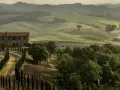 Un casale in pietra con un viale di cipressi si staglia sulle dolci colline del Val di Merse, avvolte da una leggera foschia mattutina.