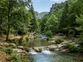 Sentiero in un bosco lussureggiante, con un fiume cristallino e una cascata. Coppia passeggia, un gruppo fa picnic. Un assaggio dei **parchi naturali Campania**.