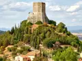 La rocca di Tentennano domina la collina, circondata da cipressi e ulivi. Sotto, un borgo con tetti rossi si adagia nel paesaggio toscano.