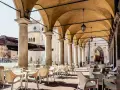Tavolini all'aperto sotto un portico con vista sul Duomo. Un'idea su cosa fare a Modena: godersi un caffè in piazza.