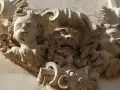Dettaglio scultoreo barocco a Martina Franca: volti di putti e una maschera grottesca emergono dalla pietra calcarea, testimoni di un'antica arte.