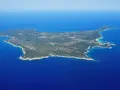 Vista aerea di un'isola verdeggiante, un'isola vicino all'Elba, con acque blu intenso e una piccola isola rocciosa in lontananza.