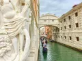 Gondole scivolano sul canale sotto il Ponte dei Sospiri, con un'imponente statua in primo piano.