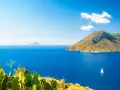 Panoramica delle Isole Eolie: cosa vedere? Un veliero solca il blu intenso del mare, con isole vulcaniche sullo sfondo e fichi d'India in primo piano.