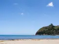 Spiaggia del Poetto con mare azzurro, montagne verdi e un porto turistico pieno di barche.