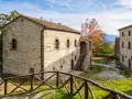 Antica strada in Casentino conduce a un borgo in pietra con un cortile interno e un albero dalle foglie arancioni.