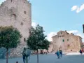 Piazza nel centro storico di Castellina in Chianti con torre medievale, edifici in pietra e scultura.