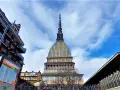 La Mole Antonelliana svetta maestosa nel cielo azzurro di Torino, circondata da edifici moderni e storici.