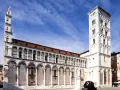 La piazza San Michele a Lucca, con la sua chiesa romanica e la torre campanaria imponente, sotto un cielo azzurro.