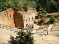 Antiche cave di tufo scavate nella roccia, con finestre e ingressi. Un gruppo di turisti esplora questo luogo affascinante, tra i **baratti cosa vedere** e la natura rigogliosa.