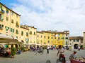 Passeggiata nella storica piazza anfiteatro di Lucca, con i suoi palazzi gialli e i tavolini all'aperto.