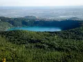 Vista panoramica del lago di Albano, circondato da rigogliosa vegetazione, con il borgo di Rocca di Papa in lontananza.