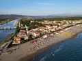 Vista aerea di Castiglione della Pescaia: un canale navigabile con barche, case con tetti rossi e una spiaggia attrezzata con ombrelloni e lettini, bagnata dal mare.