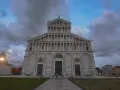 La maestosa **cathédrale de Pise** si erge sotto un cielo nuvoloso, con la sua facciata ricca di arcate e decorazioni.