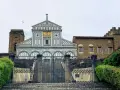 La facciata marmorea di San Miniato al Monte domina la vista, con un cancello in ferro battuto che precede la scalinata.