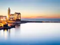 La cattedrale di Trani si erge maestosa sul mare al tramonto, illuminata da luci calde.