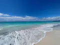 Onde turchesi lambiscono le spiagge bianche di Marina di Cecina, sotto un cielo azzurro con nuvole sparse.