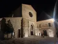 La chiesa di San Giovanni in Fiore illuminata di notte, con la sua facciata in pietra e il rosone circolare.