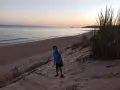 Bambino con occhiali su una duna di sabbia a Porto Palo, con il mare calmo e il cielo al tramonto sullo sfondo.
