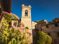 Campanile in pietra in un borgo delle Colline Metallifere, con fiori rosa in primo piano e cielo azzurro.