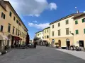 Piazza tranquilla a Pomarance, cosa vedere: edifici storici con persiane verdi, tavolini all'aperto di un bar.