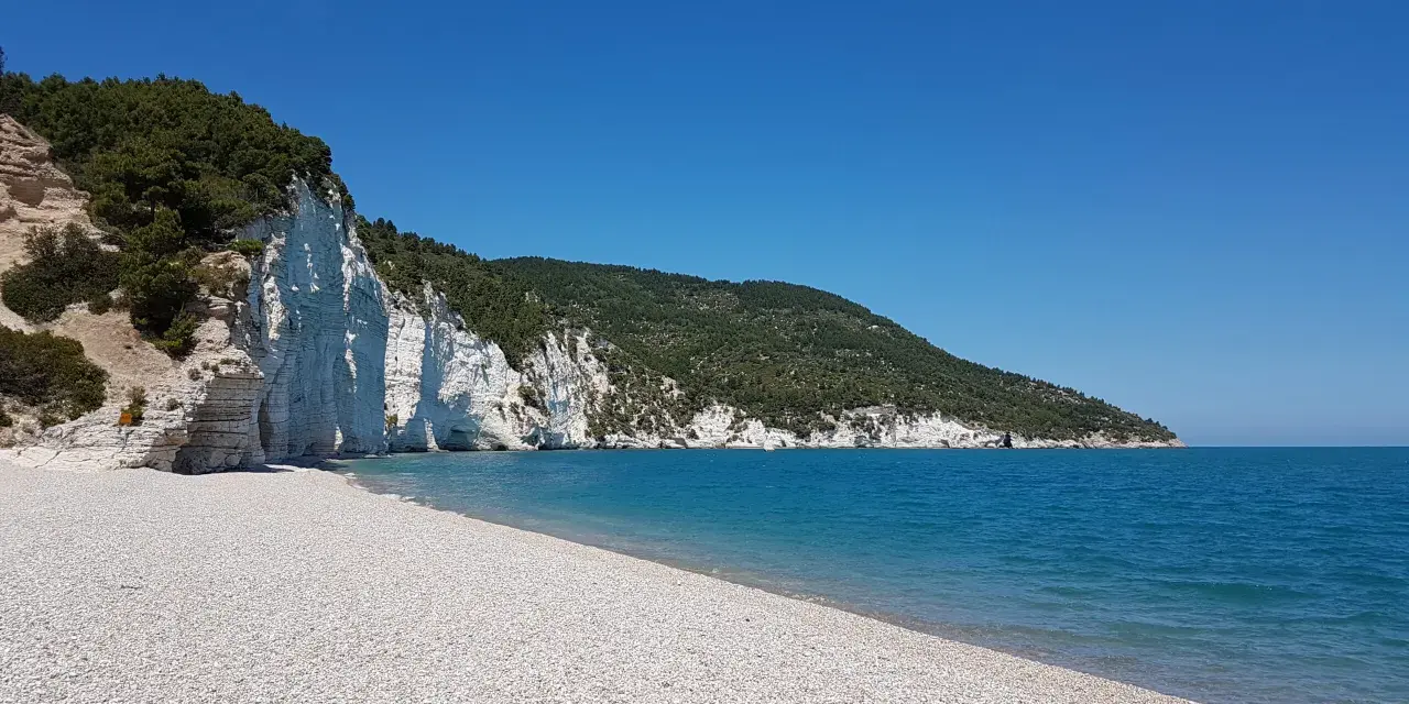 Scogliera bianca a picco sul mare turchese, con una spiaggia di ciottoli bianchi. Un angolo di paradiso, la spiaggia bianca Puglia.