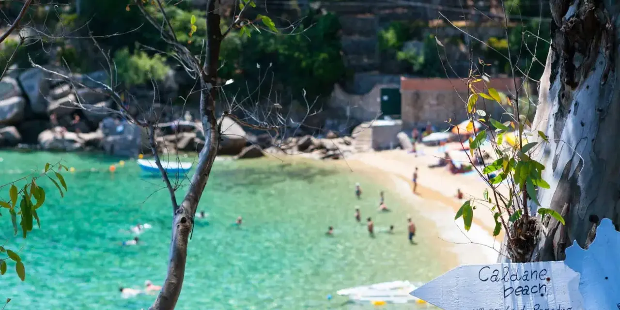 Segnale per le spiagge di Caldane, Isola del Giglio, indica un angolo di paradiso con gente che nuota nell'acqua cristallina.