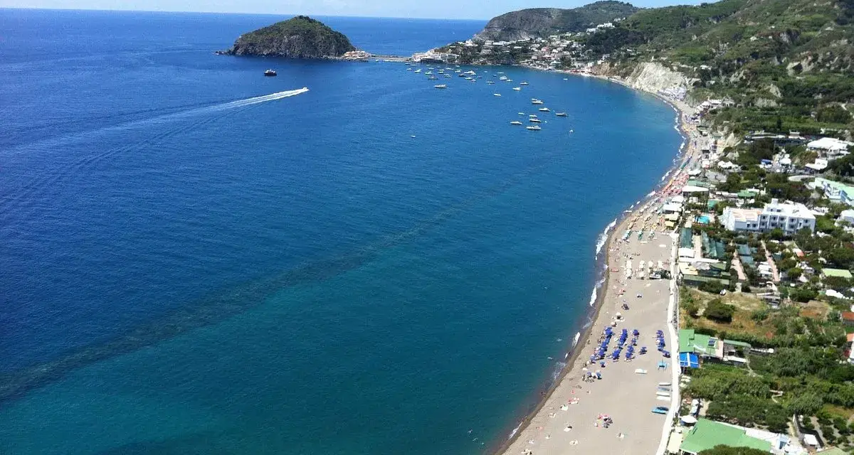 Vista panoramica della spiaggia dei Maronti, con il mare blu intenso, tante barche e la costa verdeggiante.