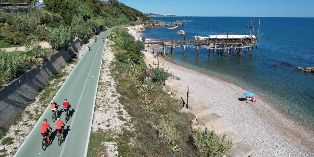 Ciclisti sulla pista ciclabile lungo mare, con i trabocchi che caratterizzano la costa dei Trabocchi cosa vedere. Spiaggia di ciottoli e mare azzurro.