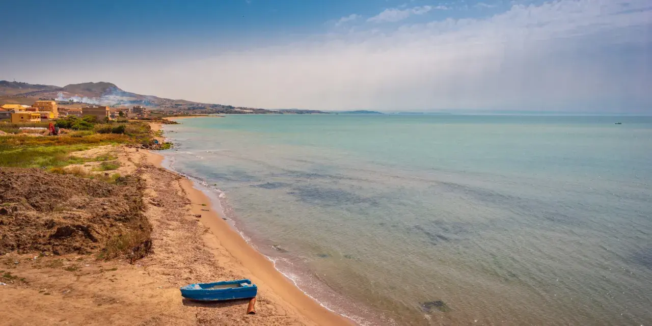 Spiaggia di Licata con barca blu e mare calmo. Un paesaggio da esplorare, tra terra e acqua cristallina.
