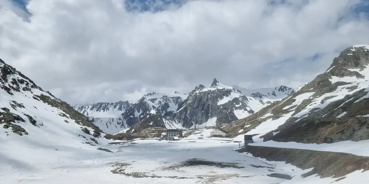 Paesaggio innevato al Gran San Bernardo con edifici storici e montagne maestose sotto un cielo nuvoloso.