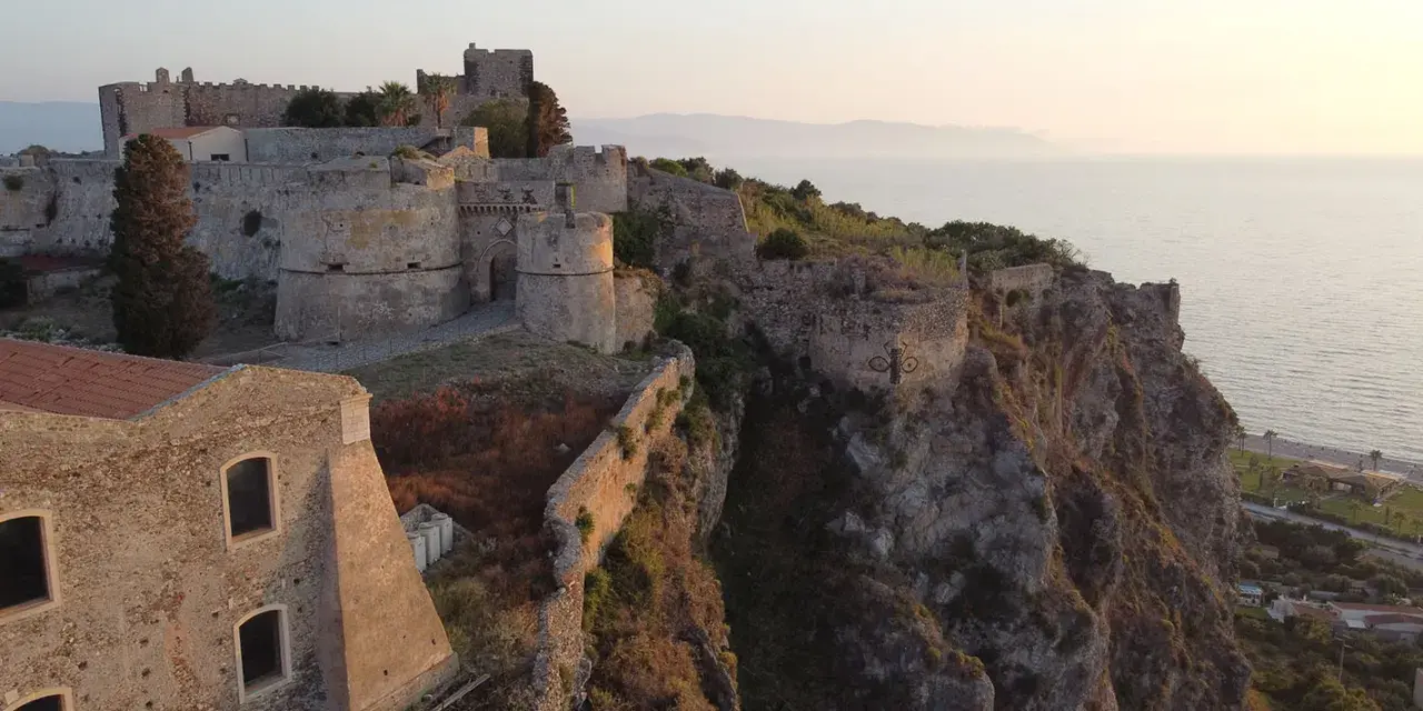 Il complesso monumentale del castello di Milazzo si erge su una scogliera a picco sul mare, con torri e mura antiche che dominano il paesaggio.