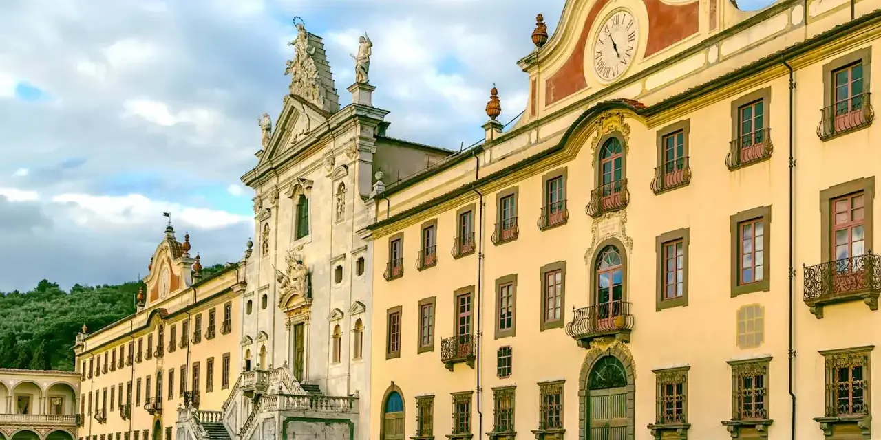 La maestosa Certosa di Calci, con la sua facciata imponente e il prato verde antistante, incanta sotto un cielo nuvoloso.