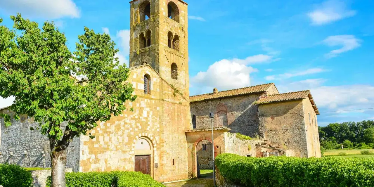 Antico campanile romanico e edifici in pietra nel **Sovicille centro storico**, con un albero verdeggiante e cielo azzurro.