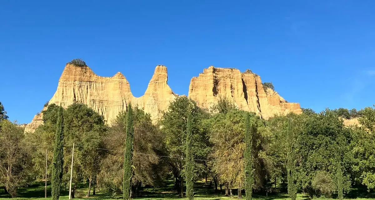 Le maestose balze del Valdarno si ergono sotto un cielo azzurro, circondate da una rigogliosa vegetazione e cipressi slanciati.